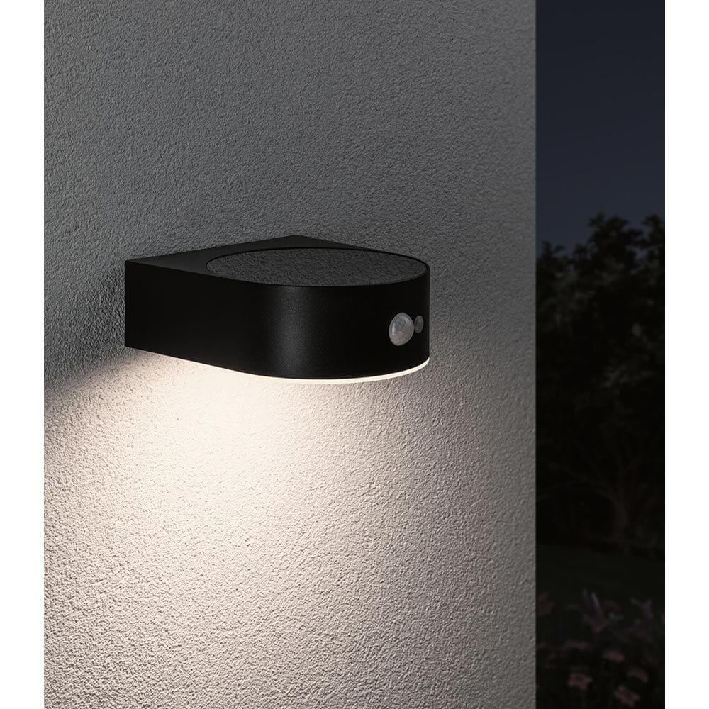 Solar LED Außenwandleuchte Eileen Sensor Schwarz an einer Wand mit warmweißem Licht.