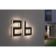 Solar LED Hausnummernleuchte Buchstabe B in Schwarz, beleuchtet an Hauswand mit warmweißem Licht.