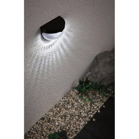 Solar LED path light Mimmo Black mounted on a wall, shining brightly in the darkness.