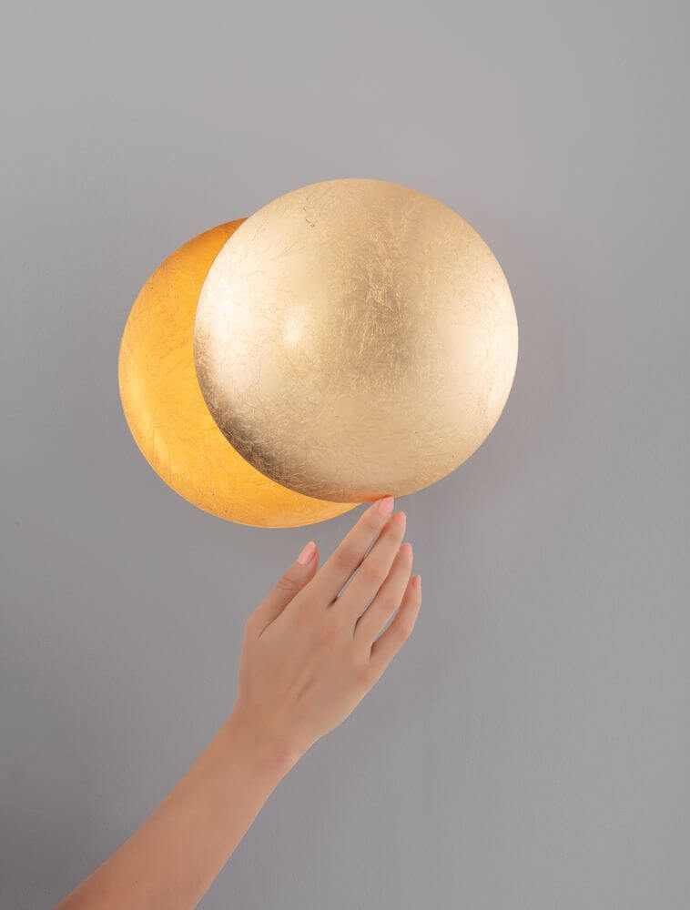 Solei LED Wandleuchte Ø 20cm, goldene Oberfläche, warmes Licht 3000K, hand berührt die Lampe an der Wand.