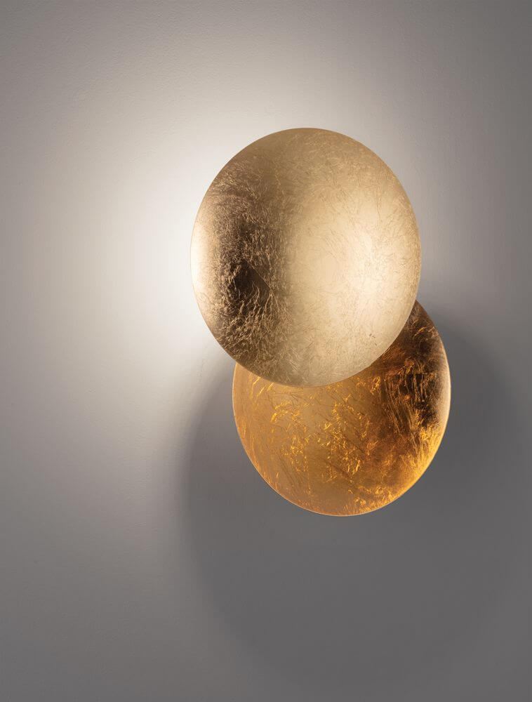 Solei LED Wandleuchte Ø 20cm in Gold mit warmem Licht (3000K) an einer grauen Wand.