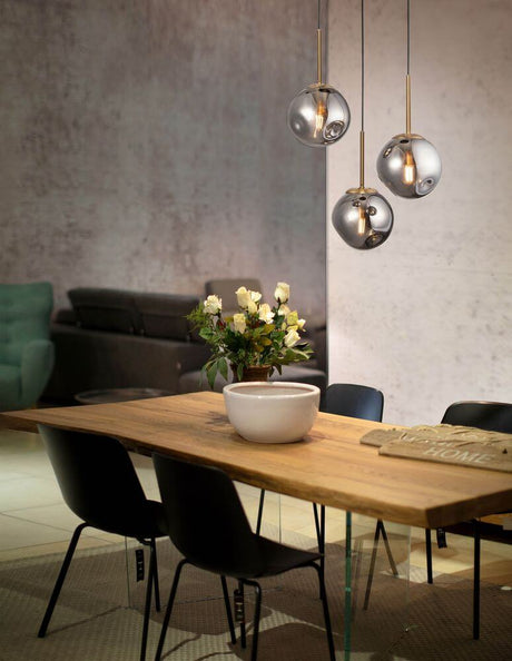 Suspension Spada à 3 lampes Ø 40 cm or, noir, fumé au-dessus d’une table à manger avec plateau en bois et boules de verre décoratives