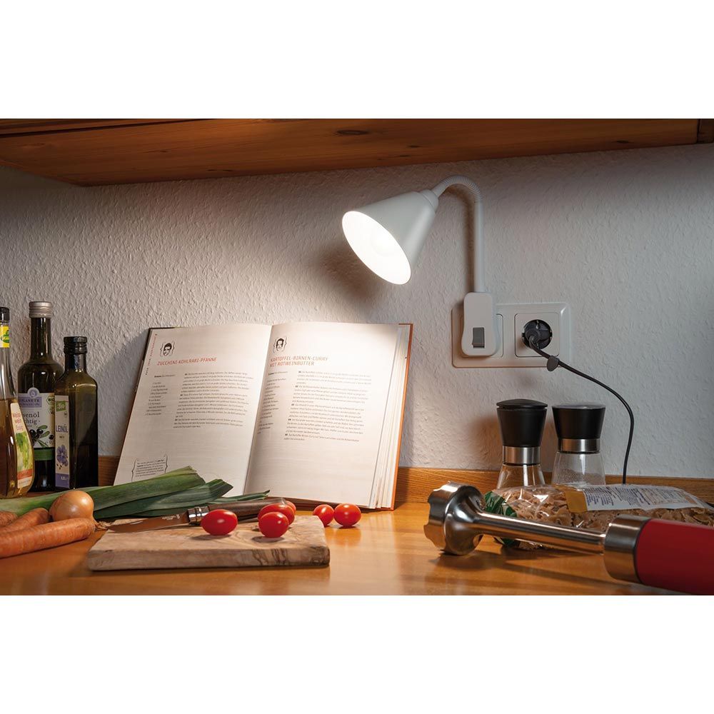 Steckerleuchte Junus Flexarm Weiß über einer Kochfläche mit offenem Rezeptbuch.