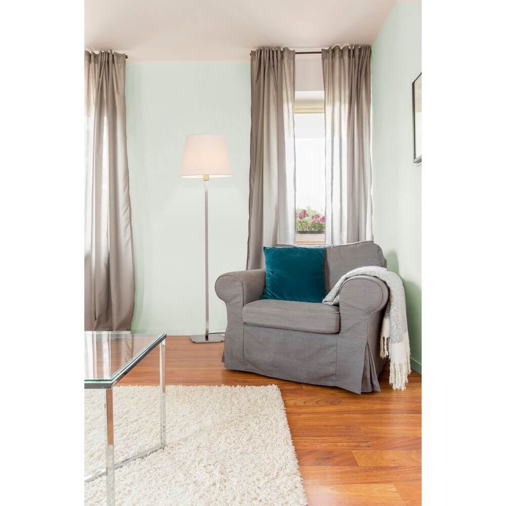 Stehlampe ESSENTIAL Nickel, Weiß in modernem Wohnzimmer mit grauem Sofa und Teppich.