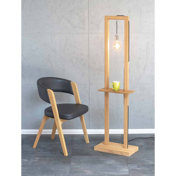 Stehlampe Monopod Eiche-Geölt neben einem modernen Stuhl und einer Tasse auf einem Tisch.