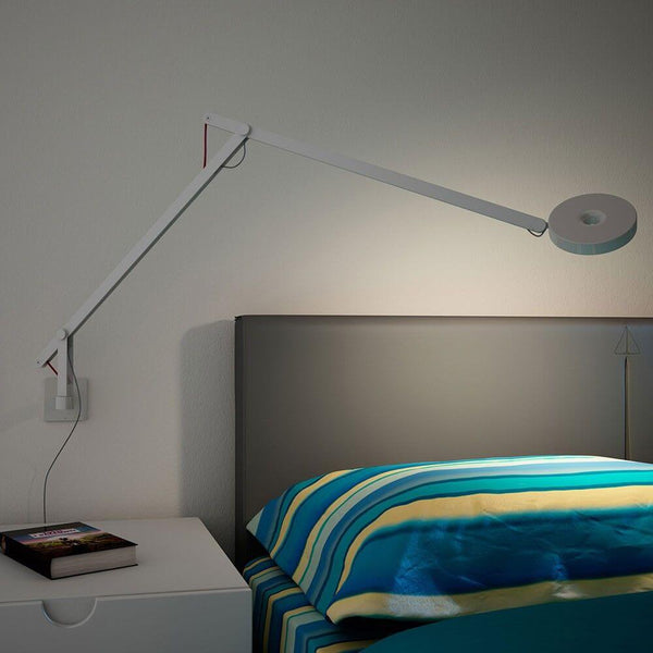 Rotaliana String LED wall light with dimmer, black, above a bed with a stack of books.