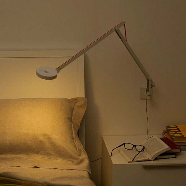 Rotaliana String LED wall light with dimmer, black, above a bed with books and glasses.