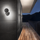 Lodes Puzzle Round Outdoor Double LED Wandlampe an einer Fassade mit Holzterrasse bei Nacht.