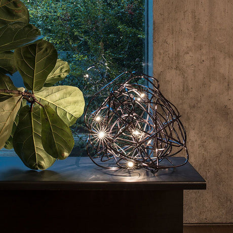 Terzani Doodle table lamp decoratively placed on a table with plants in the background.