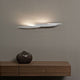 Terzani I Lucci Argentati LED Design-Wandlampe an Wand über einem Holztisch mit dekorativem Keramikgefäß.