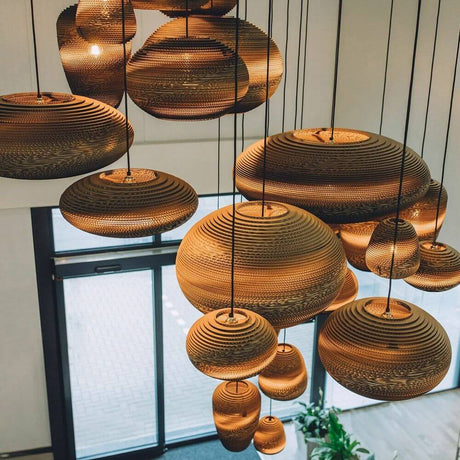 Jazzy lampe à suspendre en carton ovale, disponible en différentes tailles et formes, élégamment suspendue au-dessus d’un intérieur.