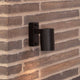 Tin Außen-Wandleuchte IP54 in Schwarz, elegant an einer Mauer montiert, ideal für den Außenbereich.