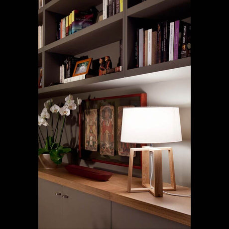 Holz Tischlampe BLISS Braun, Weiß auf einem Sideboard mit Bücherregal im Hintergrund.
