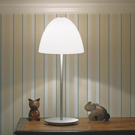 Casablanca Tischlampe Bell Ø 21cm auf einem Tisch mit Holzfiguren, sanft beleuchtet im Hintergrund.