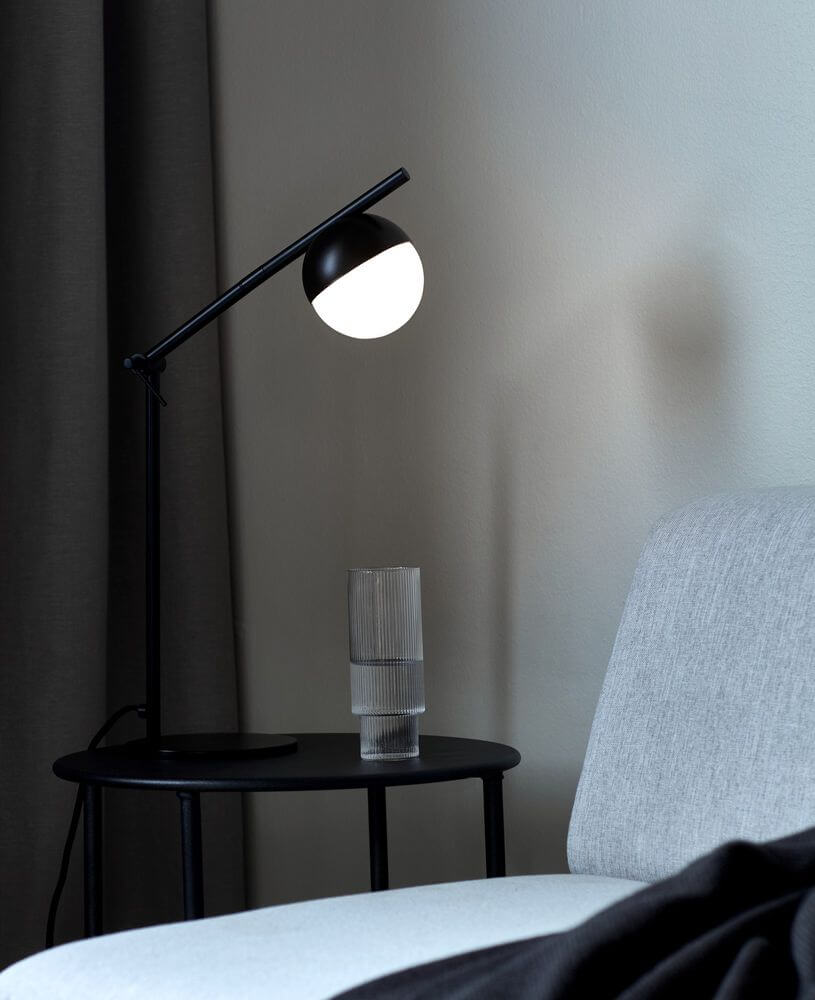 Tischlampe Contina auf einem Beistelltisch neben einem grauen Sofa mit Glaskaraffe.