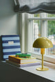 Tischlampe Ellen Mini in gelb auf einem Fensterbrett neben Büchern und Spielzeugauto.