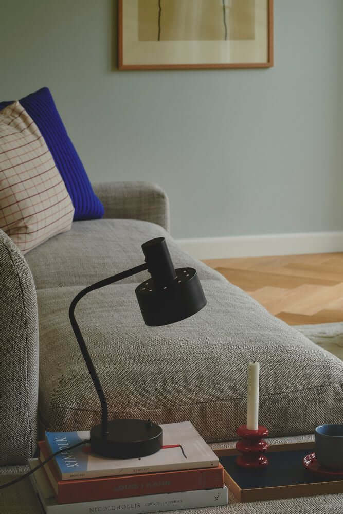 Tischlampe Matis auf einem Tisch neben einer Couch in modernem Wohnzimmer-Design.