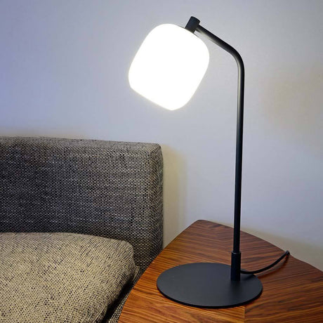 Casablanca Tischlampe Murea Ø 13cm Anthrazit auf einem Holztisch neben einer Couch.
