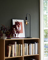 Tischlampe Paco im minimalistischen Industriedesign auf einem Regal mit Bücher und Kunstwerk.