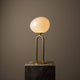 Tischlampe Shapes mit elegantem Opalglasschirm und Messingfuß auf einem Steinuntergrund.