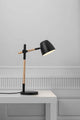 Tischlampe Theo in modernem Design mit Holz- und Metallkombination auf einem Tisch.