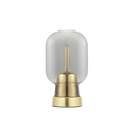 Lampada da tavolo Amp in stile scandinavo in vetro fumé, ottone su un tavolo, illuminata con una lampadina decorativa.