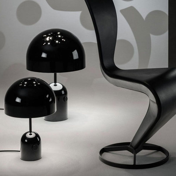 Tom Dixon Bell Tischleuchte mit Drehdimmer neben einem modernen schwarzen Stuhl in stilvollem Raum.