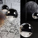 Tom Dixon Mirror Ball 5er Hängelampe in Chrom-Optik, schwebend über einem strukturierten Hintergrund.
