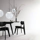 Tom Dixon Opal Kugelleuchte Pendel über einem Tisch mit schwarzen Stühlen und einem floralen Arrangement.