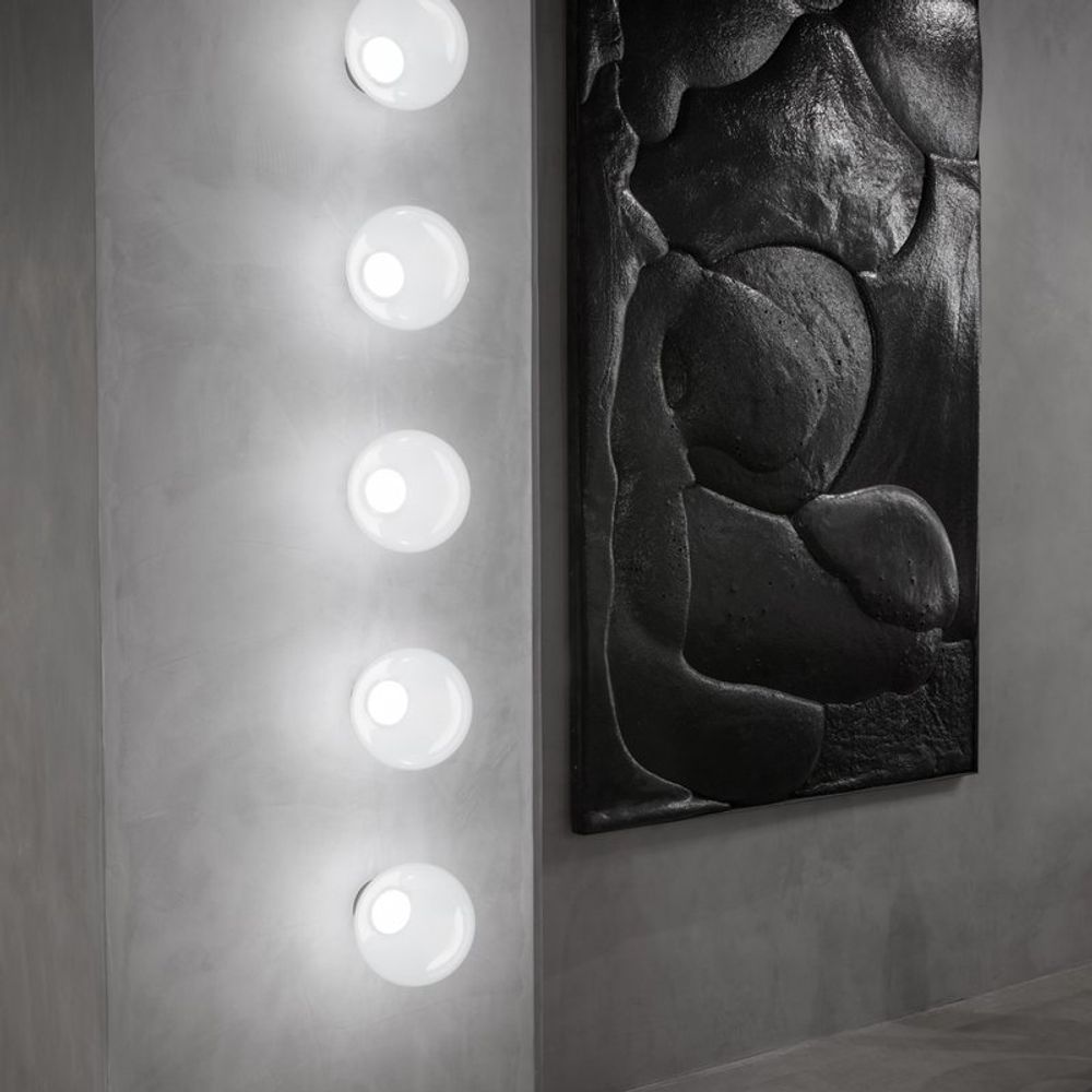 Moderne Tom Dixon Opal Wandleuchte mit sechs LED-Scheiben an einer grauen Wand, neben einem abstrakten Kunstwerk.
