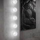 Tom Dixon Opal Wandleuchte Ø 25cm an einer grauen Wand mit modernem Kunstwerk im Hintergrund.