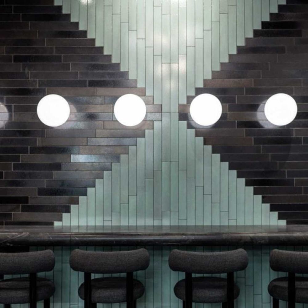 Moderne Wandleuchte von Tom Dixon auf einer stilvollen Fliesenwand mit schwarzem und grünem Design.