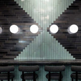 Moderne Wandleuchte von Tom Dixon auf einer stilvollen Fliesenwand mit schwarzem und grünem Design.
