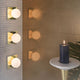 Tom Dixon Plane Wandleuchte Goldfarben an einer Fliese mit einer Kerze und Pflanzen im Hintergrund.