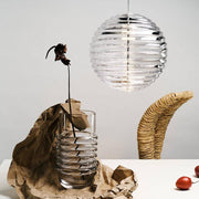 Tom Dixon Press Sphere glass pendant light above a vase with a wilted flower.