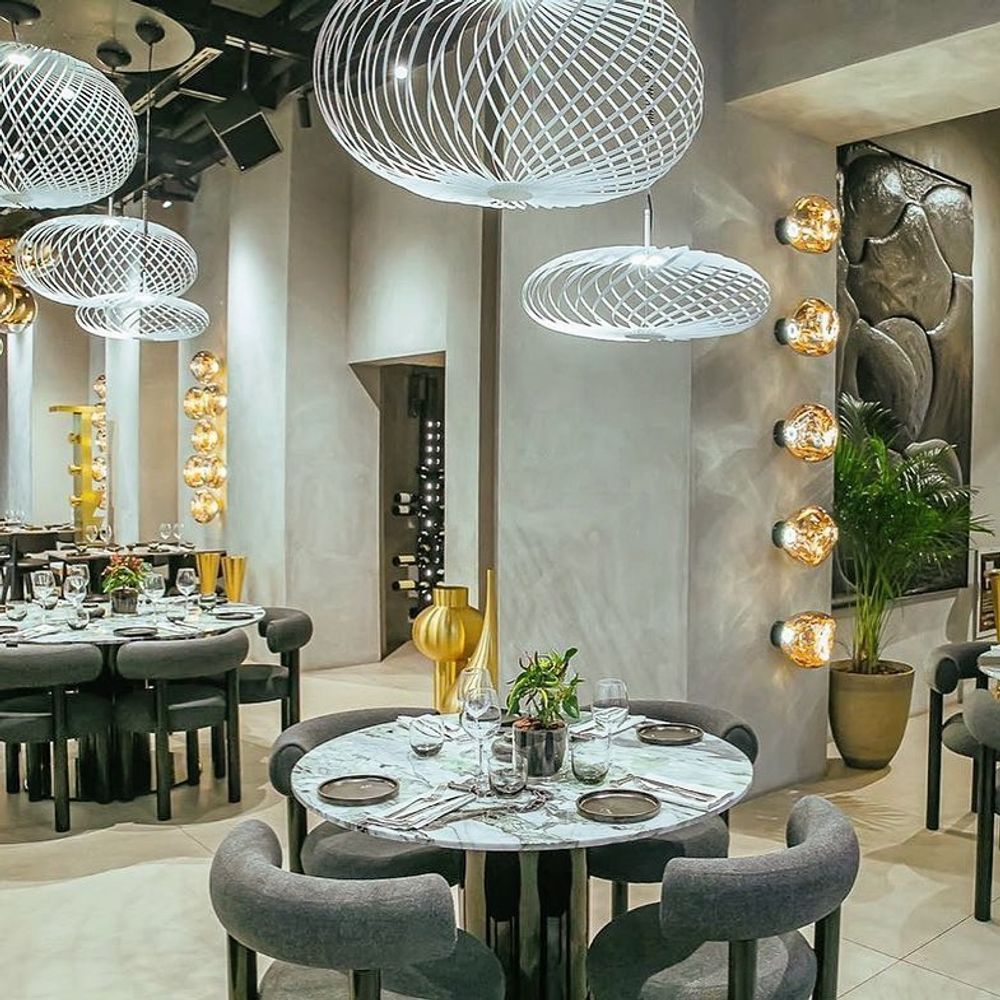 Moderne Restaurant-Atmosphäre mit Tom Dixon Spring Hängelampen und eleganten Tischarrangements.