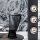 Moderne VOID Wandleuchte von Tom Dixon an einer künstlerischen Wand, ergänzt durch einen stilvollen schwarzen Stuhl.