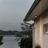 Varese LED Außen Deckenleuchte in Dunkelgrau an einem modernen Haus am Wasser, ideal für die Terrassenbeleuchtung.