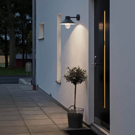 Vega LED Außen-Wandleuchte 700lm , 3000K Schwarz, klares Glas an einer Wand mit Pflanze im Außenbereich.