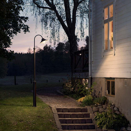 Vega LED floor lamp 700lm, 3000K black, clear glass next to a house in the garden at dusk.