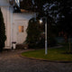 Vega Standleuchte Weiß, klares Glas leuchtet im Garten vor einem weißen Haus bei Nacht.