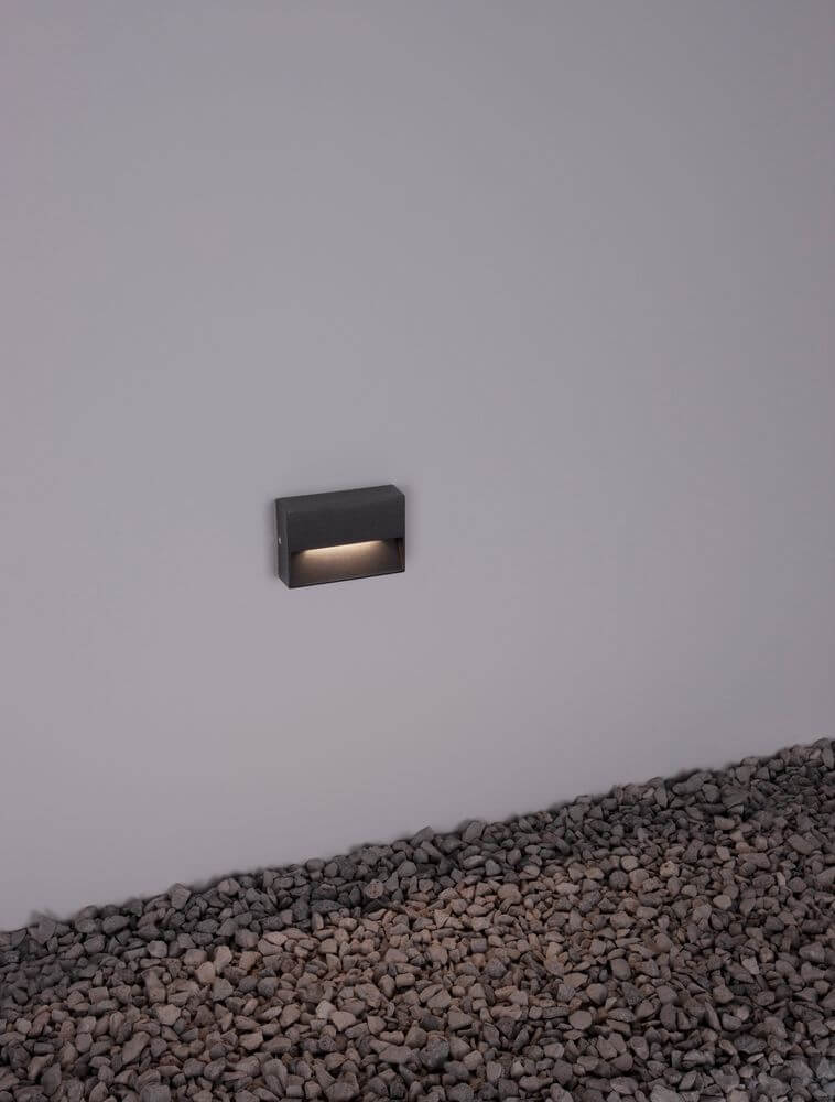 Vision LED Außenwandleuchte 3000K Anthrazit IP54 an einer Wand über Kies.