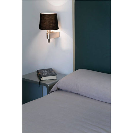 Wandlampe ROOM Nickel, Schwarz an einer Wand über einem Nachttisch mit einem Buch.