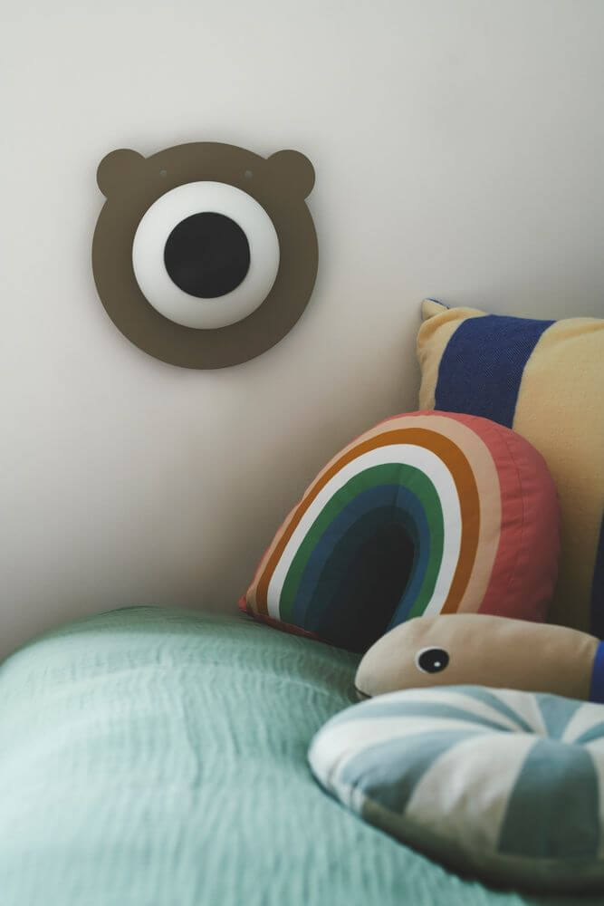 Wandleuchte Bruna Bear als niedliche Dekoration für das Kinderzimmer, mit bunten Kissen und weichem Licht.
