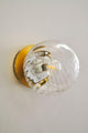 Wandleuchte Chisell mit modernem Messing und verwirbeltem Glas an einer Wand installiert.