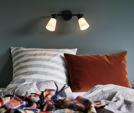 Applique murale Cole 2-Spot au-dessus d'un lit avec des coussins rayés et en velours.