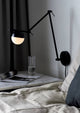 Wandleuchte Contina an einer Wand über einem Nachttisch, mit blendfreiem Licht und modernem Design.