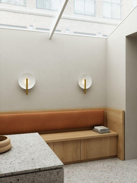 Wandleuchte Furiko an einer Wand über einer Holzbank, sorgt für sanfte, indirekte Beleuchtung im Raum.