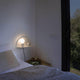 Wandleuchte Nit Weiß mit Ablagefläche neben einem Bett, gemütliche Schlafzimmereinrichtung.
