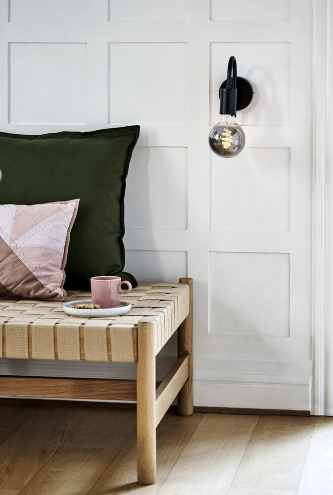 Wandleuchte Paco an einer Wand über einem Bett mit Kissen und einem Tisch mit einer Tasse.